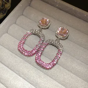 Primo piano di orecchini pendenti con strass sfumati rosa e bianchi in un portagioie grigio