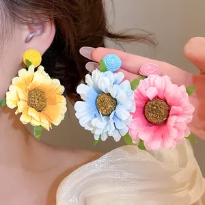 Detailweergave van handgemaakte stoffen bloemenoorbellen in geel, blauw en roze.