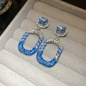 Primo piano di orecchini a pendente in argento con cristalli blu e bianchi su vassoio velluto.