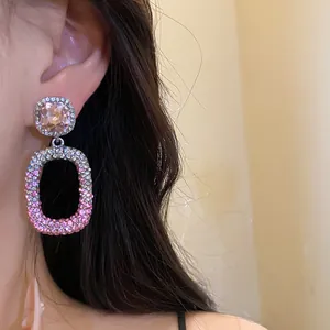 Primo piano di orecchini a sospensione con strass rosa indossati sull'orecchio