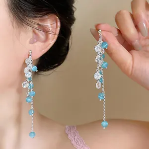 Detailed view of long silver tassel earrings with blue cat's eye beads and zircons