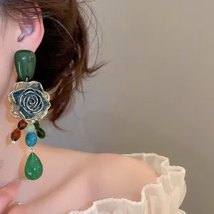 Close-up of vintage green rose earrings with dangling beads and blue rose detail.