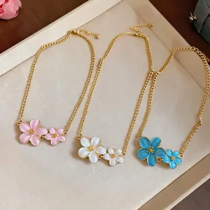Detailed view of three gold flower necklaces in pink, white, and blue on a tray.