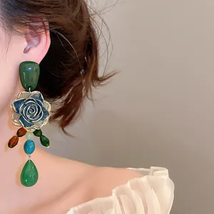 Close-up of retro green rose earrings with dangling colorful beads on a model's ear