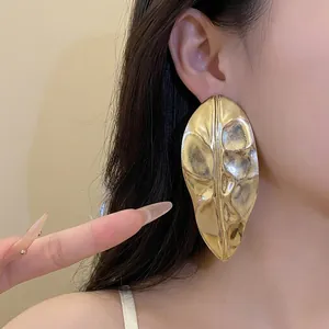 Exaggerated large gold metallic leaf earrings with a highly polished mirror finish effect