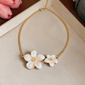 Close-up of elegant gold chain necklace with two white oil-dripped flower pendants.