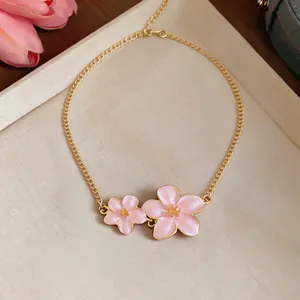 Close-up of exquisite metal necklace with pink enamel flower pendants and gold chain.
