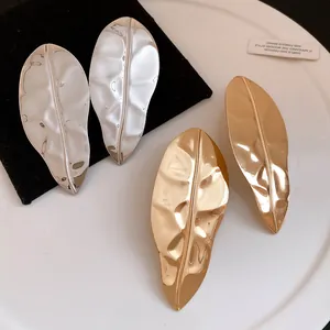Detailed macro view of glossy gold and silver leaf-shaped metal stud earrings for women