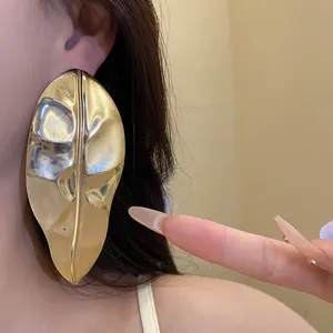 A detailed close-up of an oversized golden glossy leaf earring showing scale and texture