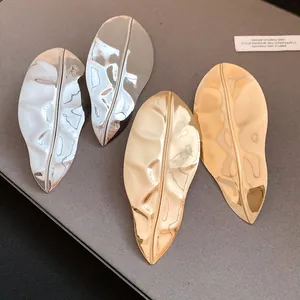 Close-up of metallic leaf-shaped earrings in gold and silver finish with textured surface