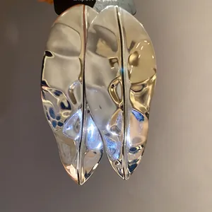 High-detail macro view of statement metallic shiny leaf earrings in silver finish.