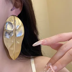 Macro detail of an oversized gold leaf-shaped earring worn on a female model's ear