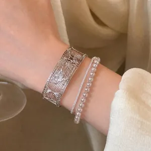 Close-up of layered silver filigree cuff with butterfly design and delicate pearl bracelet