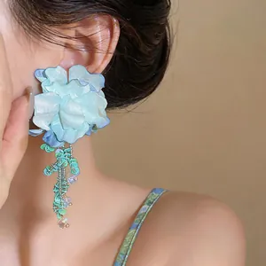 Dettaglio elegante orecchino a fiore azzurro con nappe di perline iridescenti sull'orecchio