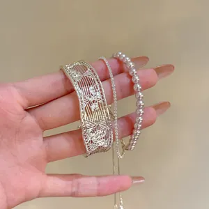 Detail shot of a silver hollow cuff, pearl bracelet, and crystal chain on a hand