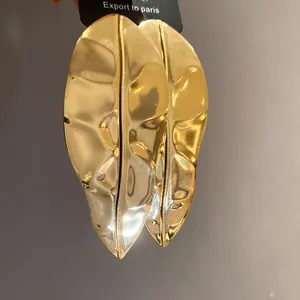 Close-up detail of oversized metallic leaf earrings in a shiny gold finish on card