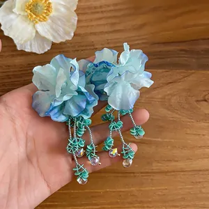 Dettaglio di orecchini a fiore blu fatti a mano con nappe di perline verdi per le vacanze.