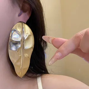 Macro view of oversized glossy gold metal leaf-shaped earrings showing a trendy style