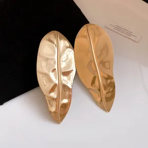 Detailed close-up view of oversized metallic gold leaf earrings with hammered texture