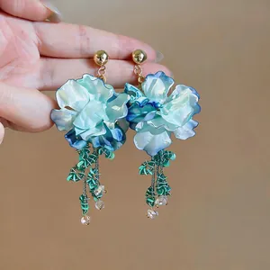 Primo piano di eleganti orecchini a fiore blu e bianchi con delicati pendenti.