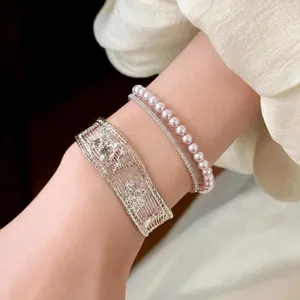 Detailed view of elegant silver openwork bangle paired with a delicate pink pearl bracelet