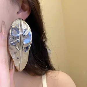 Close-up detail of an oversized metallic silver leaf earring worn on an earlobe