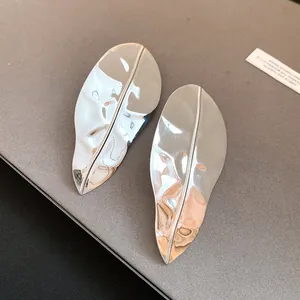 Close-up of metallic silver leaf-shaped statement earrings with a mirror finish.