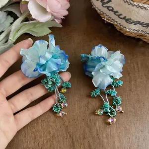 Dettaglio di orecchini a fiore in tessuto blu e bianco fatti a mano con perline