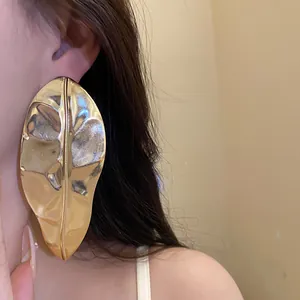 Close-up of a model wearing large metallic gold leaf-shaped statement earrings