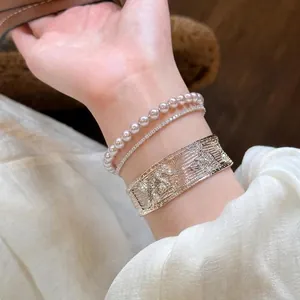 Detailed close-up of elegant silver openwork cuff and pearl bracelet stack on wrist