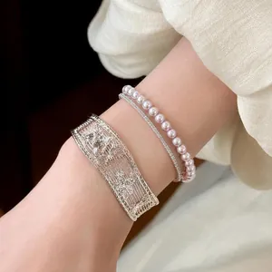 Detailed view of a silver hollow bangle, pearl bracelet, and slim crystal tennis bracelet.