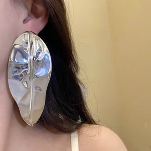 Detailed close-up view of oversized shiny silver metallic leaf earrings worn on a model