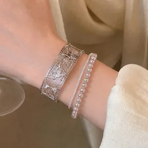 Close-up of a sophisticated silver hollow-out cuff and elegant pearl bracelet set on the wrist.