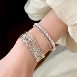 Detailed macro shot of vintage silver hollowed-out bangle and pink pearl bracelet on wrist