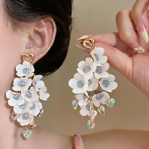 Detailed shot of elegant white fabric flower tassel earrings with golden heart studs