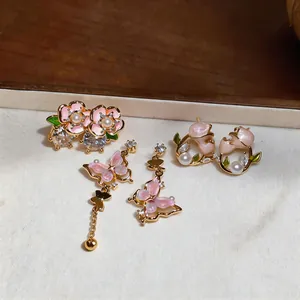 Vue détaillée des boucles d'oreilles asymétriques papillon et fleur en émail rose avec perles
