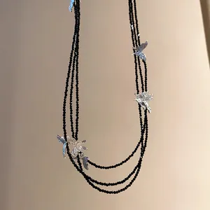 Close-up of black beaded multi-layer necklace with textured silver butterfly charms.