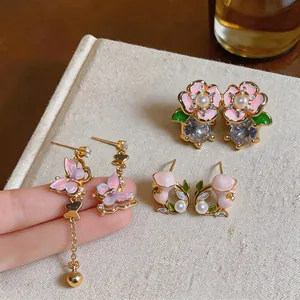 Vue détaillée des boucles d'oreilles papillon rose et fleurs sur fond en lin beige clair