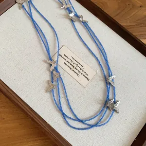 Elegant blue beaded layered necklace featuring delicate silver butterfly charms on a tray