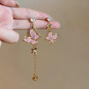 Vue détaillée de boucles d'oreilles asymétriques à pompons dorés avec papillons roses