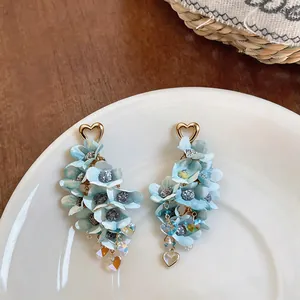 Close-up of exquisite light blue fabric flower earrings with gold heart studs and tassels