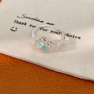 Nahaufnahme eines silbernen Rings mit einem türkisem Zirkonia-Glücksklee-Motiv auf Stoff.