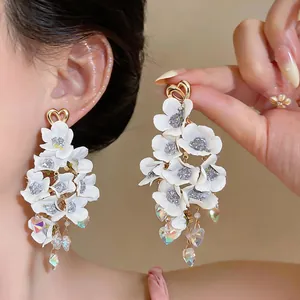 Close-up detail of elegant white fabric flower drop earrings with crystal tassels.