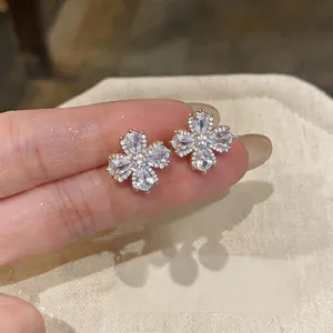 Detailed close-up view of elegant gold-plated zircon flower ear clips held between fingers