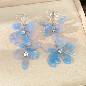 Close-up detail of blue resin flower earrings with clear heart studs and crystal centers