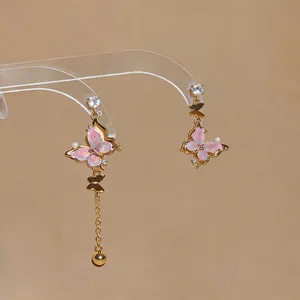 Vue détaillée de boucles d'oreilles asymétriques papillon rose avec pompon doré chic.