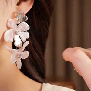 Close-up view of pink resin flower drop earrings with rhinestones on model