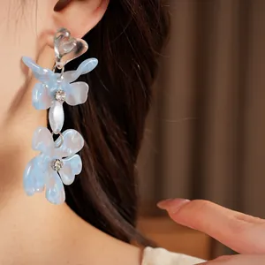 Close-up detail of light blue heart resin flower tassel earrings with rhinestones on model's ear