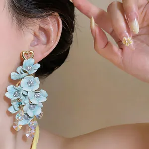 Detail view of blue fabric floral drop earrings with crystal heart pendants on model.