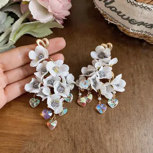 Detailed shot of white fabric flower earrings with iridescent heart-shaped crystal tassels